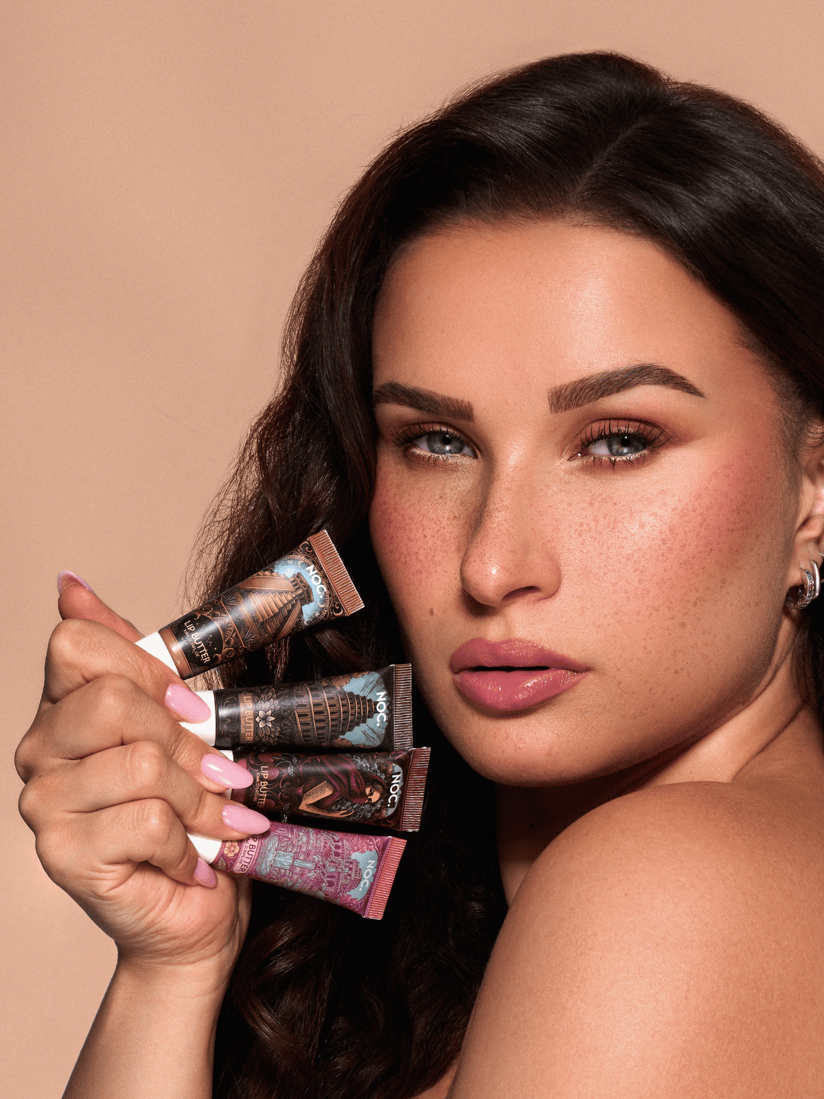 Model mit gepflegten, glänzenden Lippen hält alle 4 NOC. Lip Butter mit Peptiden